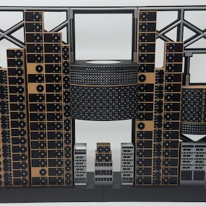 Può includere: Un modello in scala di una sala server con uno sfondo a griglia nero e grigio. La struttura comprende diverse torri verticali di rack per server neri con dettagli di ventole circolari, una grande unità cilindrica centrale e componenti rack più piccoli.