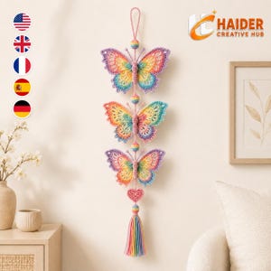 May include: A vertical wall hanging featuring three crocheted butterflies in a rainbow gradient of pink, yellow, green, and blue. The butterflies are connected by small crocheted spheres, ending with a pink heart and a multi-colored tassel.