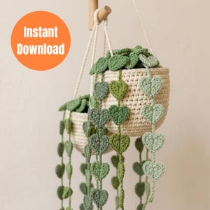 May include: Two hanging crochet plant baskets with trailing heart-shaped leaves. The baskets are a natural cream color, and the leaves are various shades of green. The text "Instant Download" is in an orange circle in the upper left corner.
