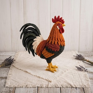 Può includere: Un gallo all'uncinetto fatto a mano nei toni dell'arancione, marrone, nero e crema. Il gallo ha cresta e bargigli rossi, zampe gialle e una coda dettagliata. È esposto su un panno color crema strutturato.