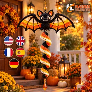 May include: A crocheted bat ornament featuring black, orange, and white yarn colors, with a spiral tail hanging below. The bat has large eyes and two white fangs. A small orange crystal bead hangs at the very bottom of the spiral tail.