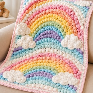 Puede incluir: Una manta de ganchillo hecha a mano con un diseño de arcoíris y detalles de nubes blancas. La manta muestra una gama de colores vibrantes, incluyendo rosa, naranja, amarillo, verde, azul y morado, con un patrón de puntada de burbuja texturizada.