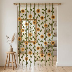 May include: A decorative crochet curtain featuring a sunflower design. The curtain is made of green yarn with yellow and brown sunflowers and green leaves. The curtain hangs from a wooden rod, creating a unique and artistic room divider.