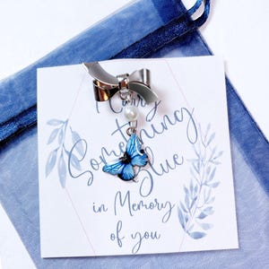 May include: A silver charm bracelet with a blue butterfly charm and a pearl bead. The charm is attached to a silver bow. The bracelet comes with a card that says "I Carry Something Blue in Memory of You".