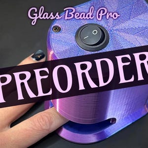 May include: A purple and blue Glass Bead Pro device with a black on/off switch. The word "PREORDER" is displayed across the device in large white letters. A hand with dark nail polish is touching the device.