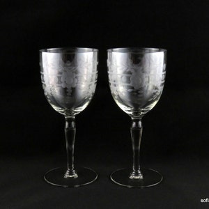 Peut inclure: Deux verres à vin transparents avec des motifs floraux gravés. Les verres ont de longues tiges et des bases rondes. Le motif gravé est visible sur le bol de chaque verre. Le fond est noir.