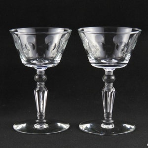 Puede incluir: Dos copas transparentes con un patrón decorativo en el cuenco. Las copas tienen una base redonda, un tallo detallado y un cuenco ancho. El fondo es negro.