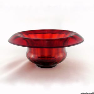 Puede incluir: Un cuenco de vidrio rojo rubí con un borde ancho y poco profundo y una base redondeada. El cuenco tiene un acabado liso y brillante. El diseño es simple y elegante, con un enfoque en el color rico y la forma. Puede usarse para fines decorativos.