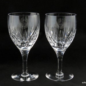 May include: A pair of clear crystal wine glasses, each with a detailed etched design. The glasses have a traditional shape, with a long stem and a circular base. The etched pattern consists of vertical and angled lines, giving a textured appearance.
