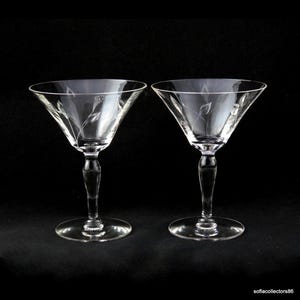 Könnte beinhalten: Zwei klare Martini-Gläser mit geätzten Blattmustern. Die Gläser haben eine klassische V-Form, schlanke Stiele und runde Basen. Der Hintergrund ist schwarz und hebt die elegante Glasware hervor.