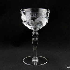 May include: A clear, stemmed glass with etched floral designs. The glass features a round base, a slender stem, and a bowl-shaped top. The etched patterns include leaves and other botanical elements. The glass is likely used for serving beverages.