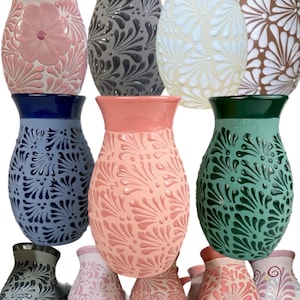 May include: A collection of ceramic vases in various colors, including pink, blue, green, and gray. Each vase features embossed floral or leaf patterns. The vases have a glossy finish and are suitable for home decor.