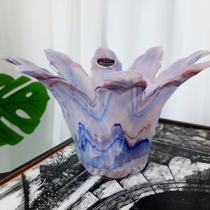 Könnte beinhalten: Eine Murano-Glasvase mit einer einzigartigen, blütenartigen Form. Die Vase weist eine Mischung aus Farben auf, darunter Blau-, Lila- und Rottöne, wodurch ein marmorierter Effekt entsteht. Das Glas ist durchscheinend und lässt Licht durch. Ein kleines Etikett ist an der Vase angebracht.
