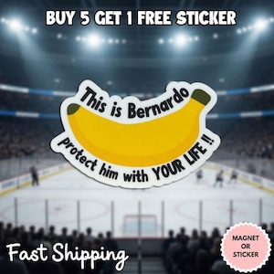 May include: A die-cut sticker featuring a yellow banana illustration with dark brown tips. The text reads, This is Bernardo protect him with YOUR LIFE !! in black lettering. The sticker has a white border and is presented against a blurred arena.