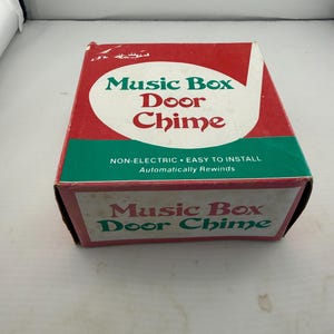May include: A rectangular cardboard box for a Music Box Door Chime. The box features a red and green color scheme with white text reading Music Box Door Chime, Non-Electric, Easy to Install, and Automatically Rewinds on the front and side panels.