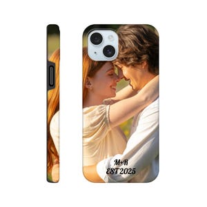 May include: A personalized phone case featuring a couple embracing, with the text "M+R EST2025" in a script font. The case has a black border and a glossy finish, showcasing a vibrant photo of the couple.
