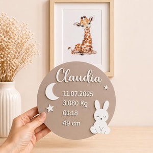 Könnte beinhalten: Runde, taupefarbene Plakette mit dem Namen "Claudia" in weißer Schrift. Sie zeigt einen weißen Mond, Sterne und ein Häschen. Die Plakette zeigt auch Datum, Gewicht (3.080 kg), Uhrzeit und Größe (49 cm).