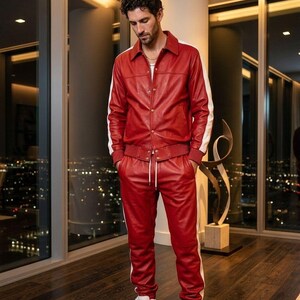 May include: A red leather tracksuit with white stripes on the sleeves and sides of the pants. The jacket has a collared neckline and button closure. The pants have a drawstring waist. The person is wearing white sneakers.