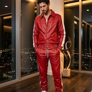 May include: A red leather tracksuit with white stripes on the sleeves and sides of the pants. The jacket has a collared neckline and button closure. The pants have a drawstring waist. The outfit is paired with white sneakers.