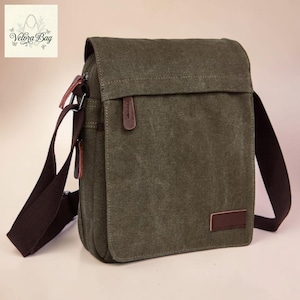 Peut inclure: Sac messager en toile vert olive avec une bandoulière réglable marron et des détails en cuir marron. Le sac a une fermeture à rabat et un petit patch en cuir marron à l'avant. Le texte "Velora Bag" est visible en haut à gauche.