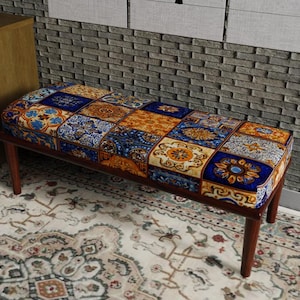 May include: A rectangular bench with a patchwork design seat in shades of blue, orange, and gold. The bench has a dark brown wooden frame and four legs. The bench is placed on a patterned rug.