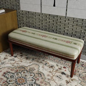 May include: A rectangular bench with a padded seat featuring a striped pattern in green, red, and cream. The bench has a dark brown wooden frame and legs. The bench is placed on a patterned rug.