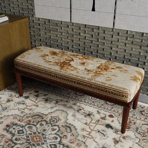 May include: A rectangular bench with a floral patterned cushion and dark brown wooden legs. The cushion features a cream background with large brown flowers and a decorative border. The bench is placed on a patterned rug.