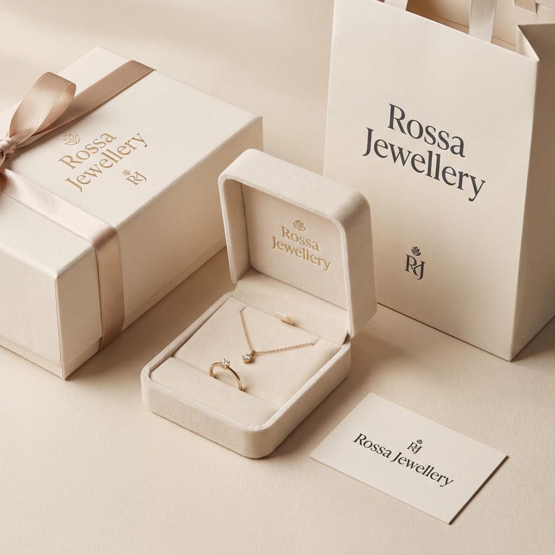 May include: An open jewelry box with a gold ring and necklace with a diamond pendant. A matching gift box with a ribbon, a shopping bag, and a card with the text "Rossa Jewellery" are also present. The items are displayed on a cream-colored surface.