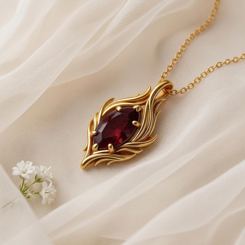 May include: A gold-colored pendant necklace featuring a large, oval-shaped, deep red gemstone. The gemstone is set in a decorative gold frame with a leaf-like design. The necklace chain is also gold.