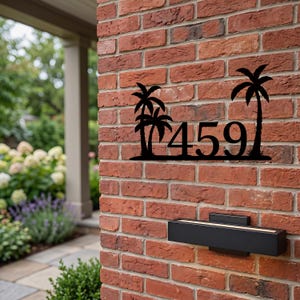 May include: Black metal address sign with the number 459 and palm tree silhouettes. The sign is mounted on a red brick wall, with a black light fixture below.