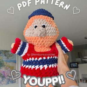 May include: A crocheted doll with a round head and body. The doll features a blue hat, orange face, and a red, white, and blue outfit. The image includes the text "PDF PATTERN" and "YOUPPI!", along with the Instagram handle "@kimbuns.crochet".