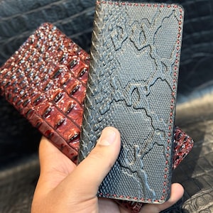 May include: Two leather wallets. One is black with a snakeskin pattern and red stitching. The other is a reddish-brown with a crocodile skin pattern. Both wallets are rectangular and appear to be bi-fold.
