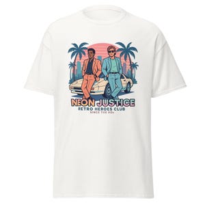 Può includere: T-shirt bianco con una grafica retrò di due persone appoggiate a un'auto, palme e un paesaggio urbano. Il design include il testo "NEON JUSTICE RETRO HEROES CLUB SINCE THE 80S".