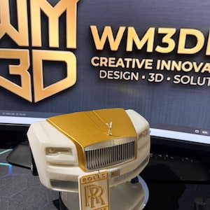 May include: A 3D printed model of a white and gold Rolls-Royce car front featuring a prominent vertical grille, a hood ornament, and a rectangular license plate with the text ROLLS ROYCE and the double R logo centered on the front bumper.