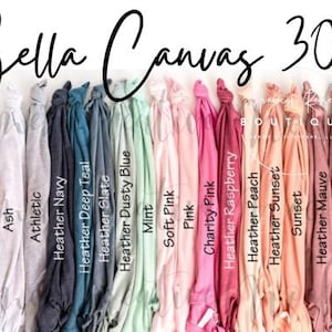 May include: A collection of Bella Canvas 3001 t-shirts displayed in a row, featuring a wide spectrum of colours including black, grey, white, blue, teal, mint, pink, peach, and maroon, with each shirt labelled by its specific colour name.