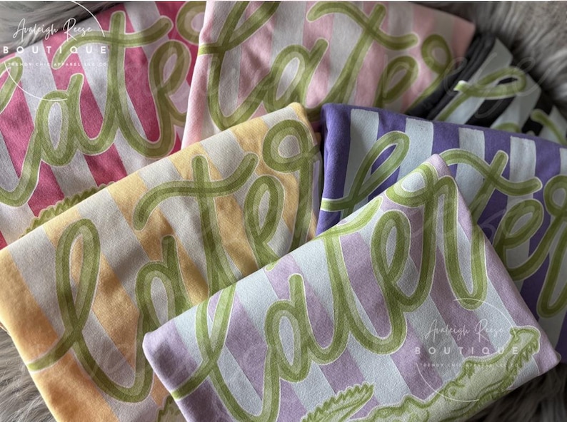 May include: Folded t-shirts in various pastel colors, including pink, yellow, and purple, with a striped pattern. Each shirt features the word "Easter" in green script. The shirts are from the Analeigh Reese Boutique.