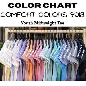 May include: A color chart of Youth Midweight Tees in various colors, including white, butter, and black. The shirts are displayed on hangers, showcasing the range of available hues. The text "COLOR CHART" and "COMFORT COLORS 9018" are visible.