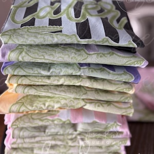 May include: A stack of folded t-shirts with a striped design and the word "CATCH" in green script. The shirts are in various colors, including black, white, pink, and yellow. The image also includes the text "Avaleigh Reese Boutique".