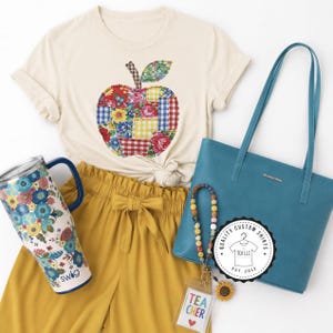 May include: A cream-colored t-shirt featuring a patchwork apple graphic, mustard yellow paper-bag waist pants, a teal tote bag, a floral-patterned tumbler with a handle, and a beaded lanyard with a clear ID holder labeled TEACHER.