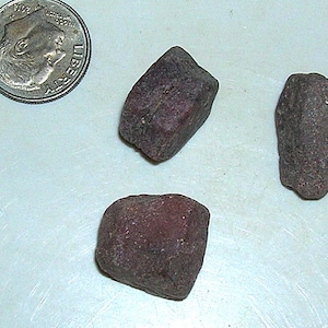 May include: Three dark red, rough, irregularly shaped stones. The stones are about the size of a dime.