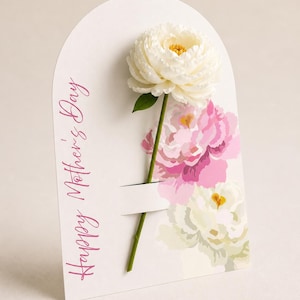 May include: A white Mother's Day card with a large white peony and a green stem. The card has a cutout to hold the flower and features the text "Happy Mother's Day" in pink script. Pink and white floral illustrations are in the background.