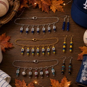 May include: Three charm bracelets and three pairs of drop earrings featuring baseball team themes. The bracelets display the words DODGERS, BREWERS, and D-BACKS using letter beads and colored accents. The earrings feature matching bead color schemes.