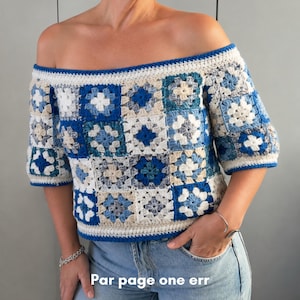 Peut inclure: Un haut en crochet à épaules dénudées composé de motifs carrés dans des tons de bleu, blanc et beige. Le vêtement présente des manches courtes et une bordure bleue unie le long de l'encolure et de l'ourlet. Le texte "Par page one err" est visible.