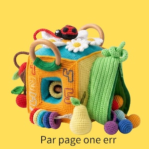 Peut inclure: Un cube sensoriel en crochet multicolore avec une coccinelle, des marguerites blanches, des anneaux en bois et une pochette verte zippée. Le cube présente des chiffres brodés et des fruits en crochet comme une poire et des cerises. Texte : Par page one err.