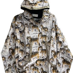 May include: White hooded sweatshirt featuring a repeating pattern of wolves in a snowy landscape. The design includes brown and gray wolves. The hood and pocket edges are trimmed with a gold Greek key pattern. The sweatshirt has a black interior.
