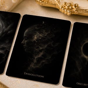 May include: Three tarot cards with black backgrounds and gold detailing. The central card shows a profile of a face with the word "Dissolution" beneath. The other cards have abstract designs and the word "Obscurity".