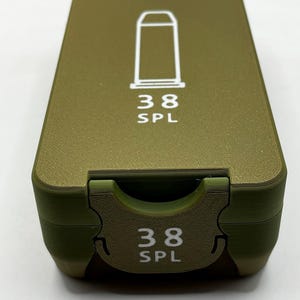 May include: Olive green rectangular case with a white graphic of a bullet and the text "38 SPL". The case has a hinged lid and a matching clasp. The case is designed to hold ammunition.
