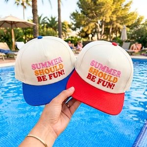 Op de afbeelding: Twee gebroken witte baseballpetten met de geborduurde tekst SUMMER SHOULD BE FUN! in roze, oranje en rood. De ene pet heeft een blauwe klep en een blauwe knoop bovenop, de andere heeft een rode klep en een rode knoop bovenop.