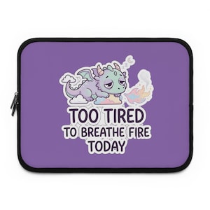 May include: A purple laptop sleeve with a black border. The sleeve features a cartoon dragon with a sleepy expression, sitting on a cloud. Text on the sleeve reads "TOO TIRED TO BREATHE FIRE TODAY."