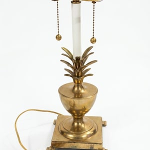 May include: A brass pineapple-shaped table lamp with a clear acrylic center column. The lamp has two light sockets with pull chains and a square base. The cord and plug are visible.